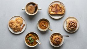 グレーのコンクリートの上に並べた、シナモンを使ったコーヒー、トースト、クッキー、カレー、焼きりんごを真上から